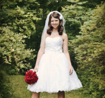 Bride in a tea-length lace gown holding a red rose bouquet in the woods