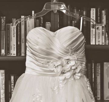 Ivory wedding dress with beaded floral detail hanging in front of a bookshelf