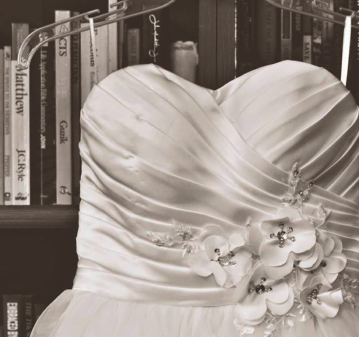 Ivory wedding gown bodice with a beaded floral appliqué, hanging in front of a bookshelf